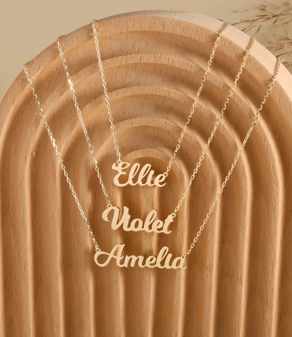 Gold necklaces with 'Ellie,' 'Violet,' and 'Amelia' nameplate pendants on a wooden background.