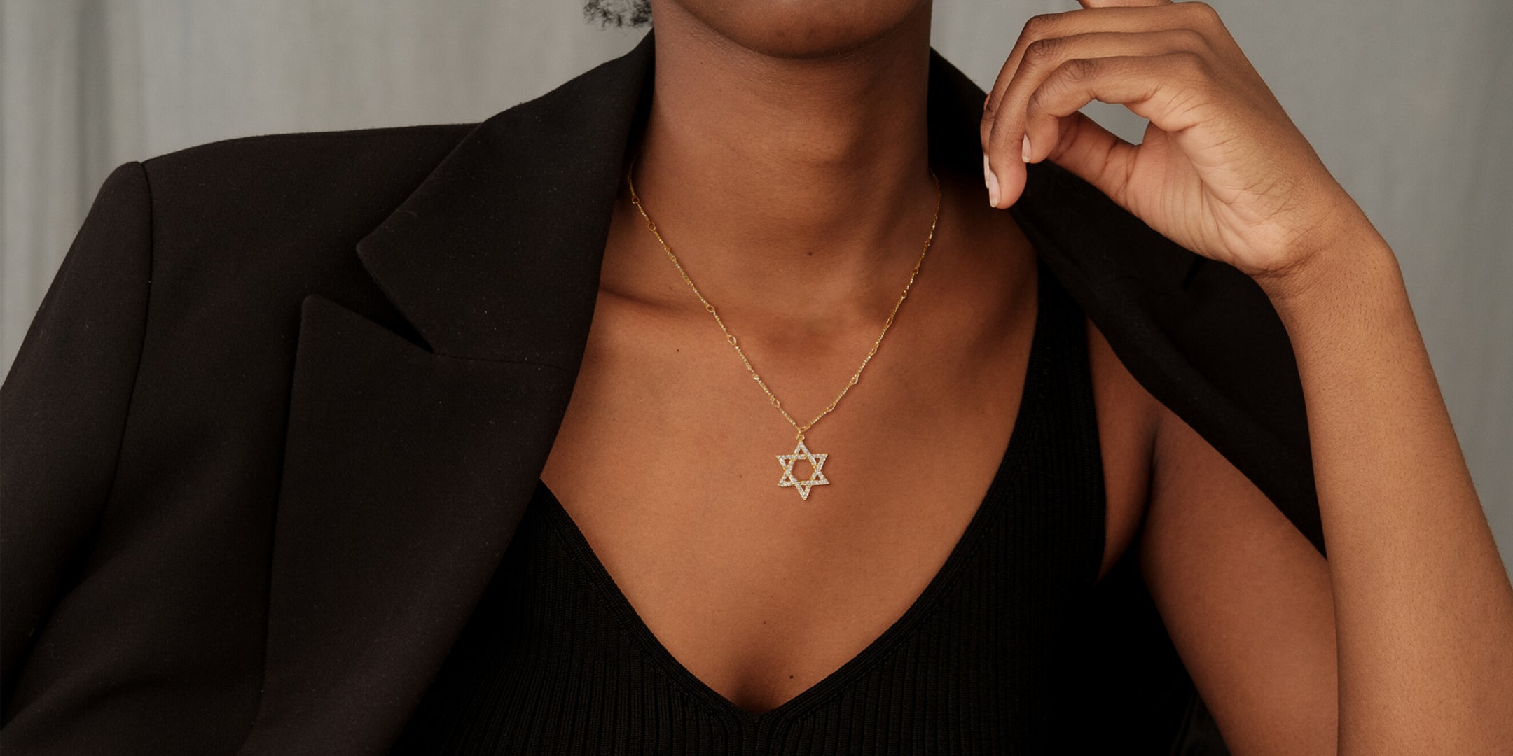 Woman wearing a gold Star of David necklace with a black top and blazer.