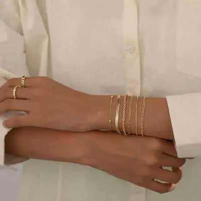 Woman wearing gold layered bracelets and a ring, white shirt, fashion jewelry.