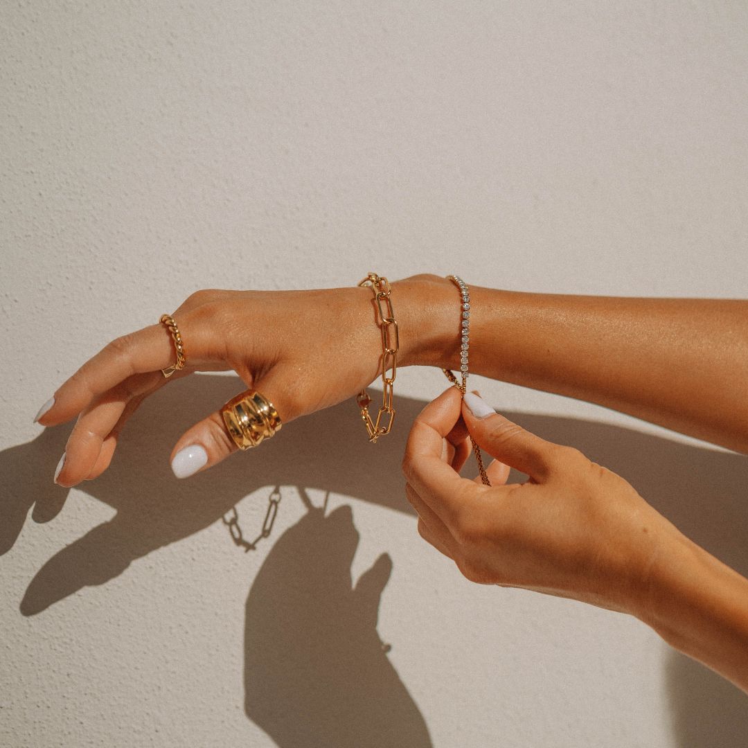 Woman's hands wearing gold rings and bracelets against a white background.