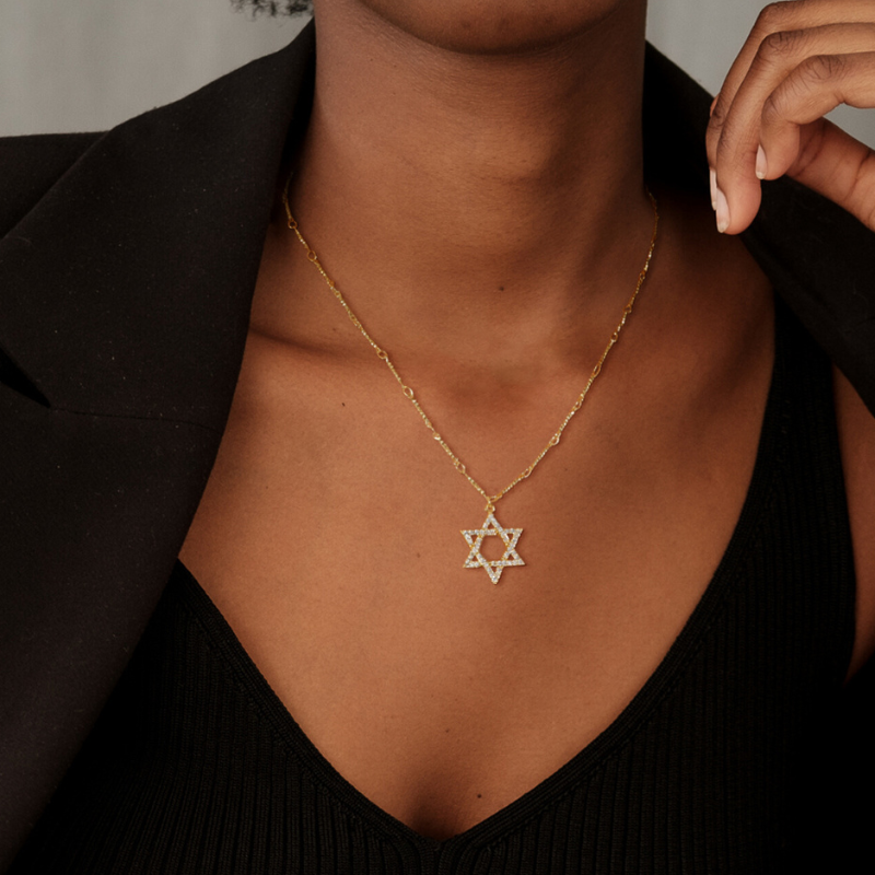 Woman wearing a gold Star of David necklace with a black top and blazer.