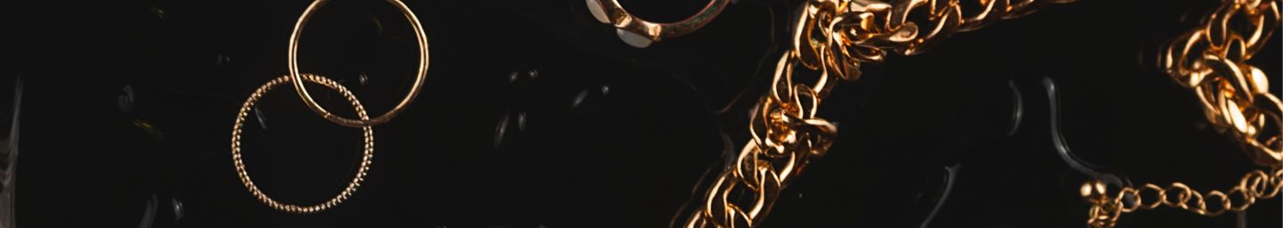 Gold jewelry pieces including rings and chains on a black background.