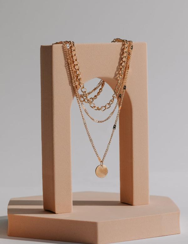 Layered gold necklaces displayed on a beige stand.