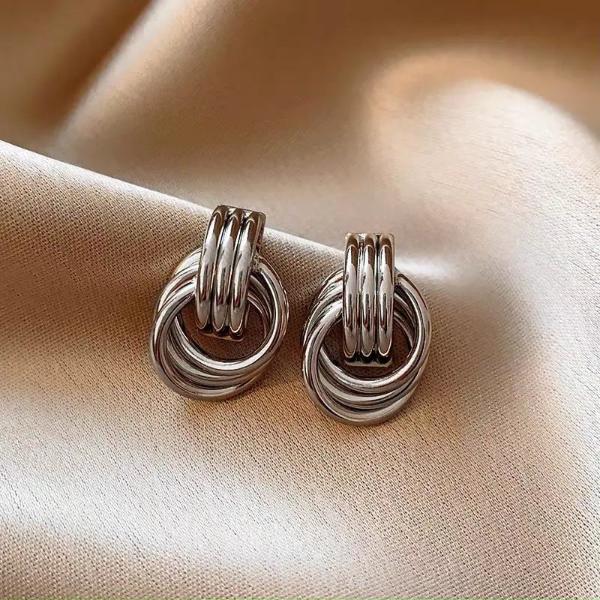 Silver knot earrings on a satin background.